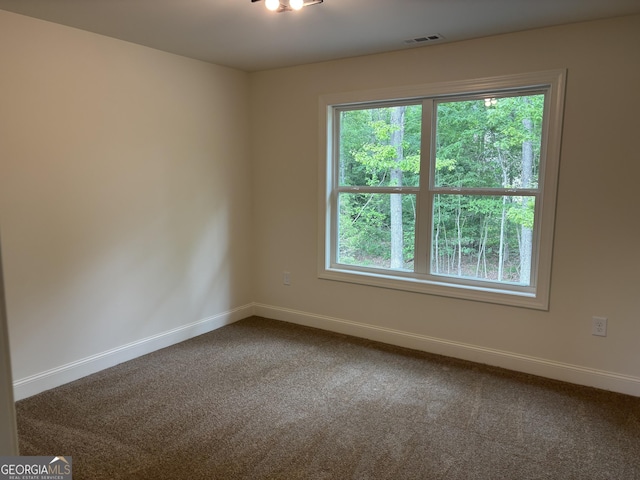 spare room with dark colored carpet, baseboards, and visible vents