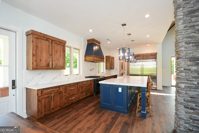 kitchen with dark wood-type flooring, premium range hood, a kitchen island with sink, backsplash, and white range with gas cooktop