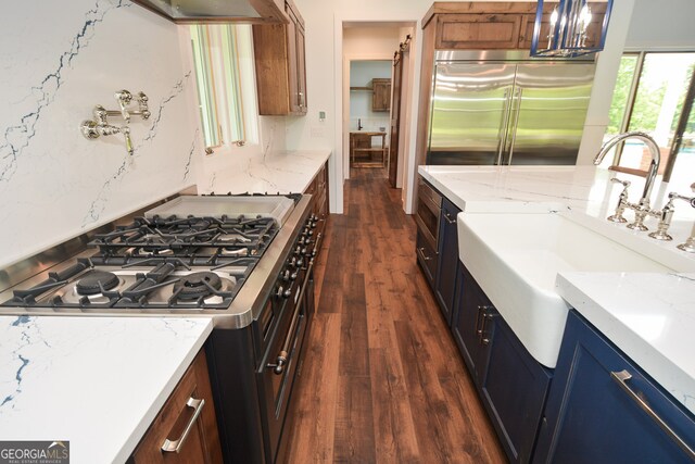 kitchen featuring stainless steel built in refrigerator, dark hardwood / wood-style flooring, gas range oven, wall chimney exhaust hood, and sink