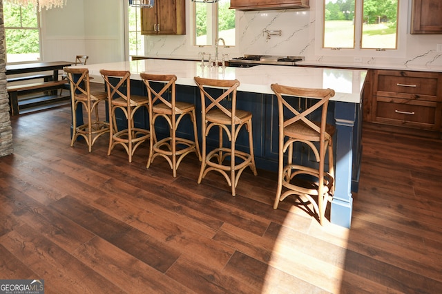 kitchen with a center island, a kitchen breakfast bar, light stone counters, and dark hardwood / wood-style flooring