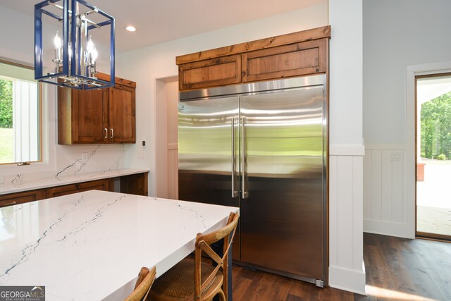 kitchen with dark hardwood / wood-style floors, light stone countertops, stainless steel built in fridge, hanging light fixtures, and a chandelier