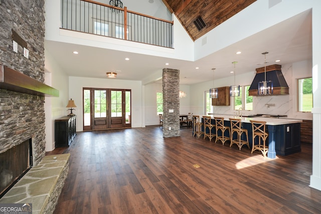 living room with high vaulted ceiling, a stone fireplace, a chandelier, and dark wood-type flooring