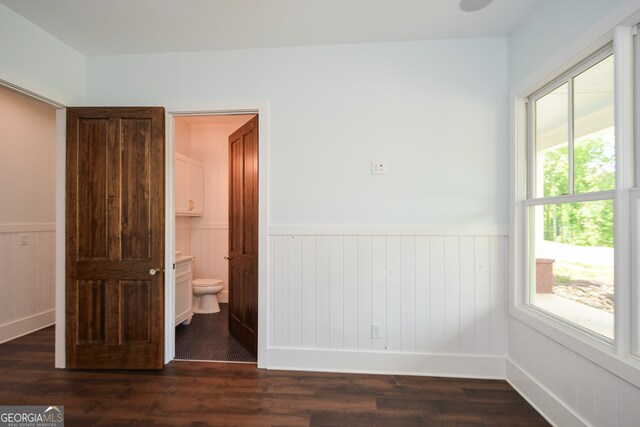 unfurnished bedroom featuring ensuite bathroom and dark hardwood / wood-style flooring