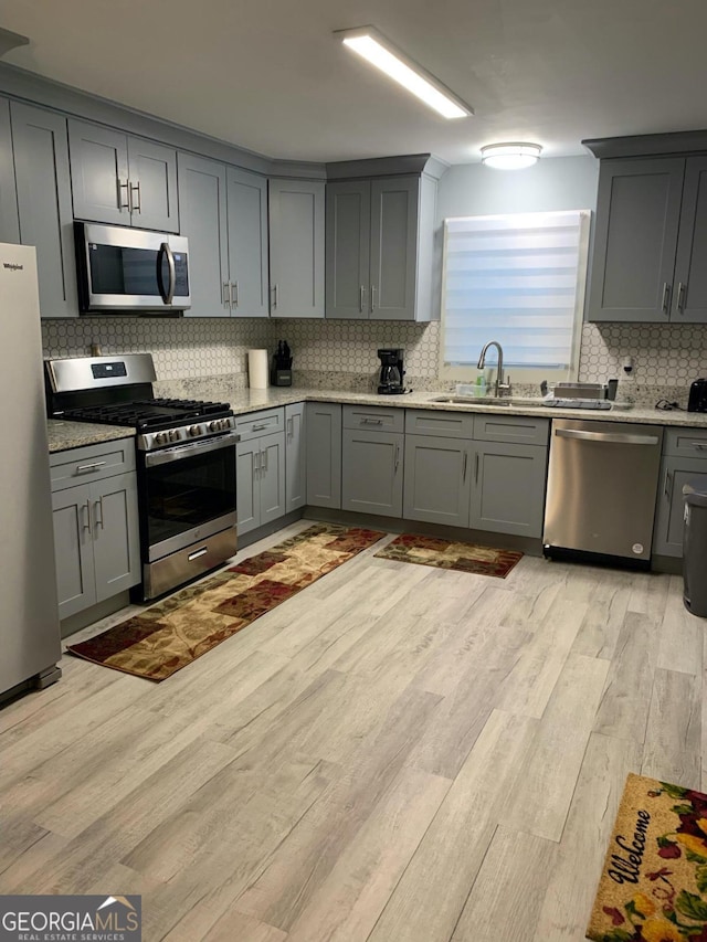 kitchen featuring gray cabinetry, sink, stainless steel appliances, tasteful backsplash, and light wood-type flooring