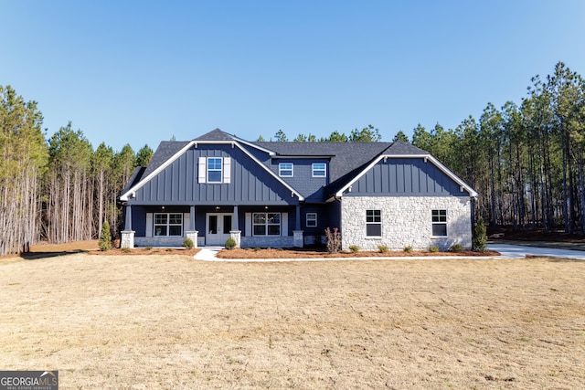 view of front of house with a shingled roof, stone siding, covered porch, board and batten siding, and a front yard