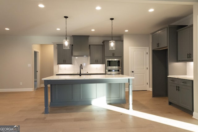 kitchen with light countertops, appliances with stainless steel finishes, gray cabinets, and a kitchen island with sink