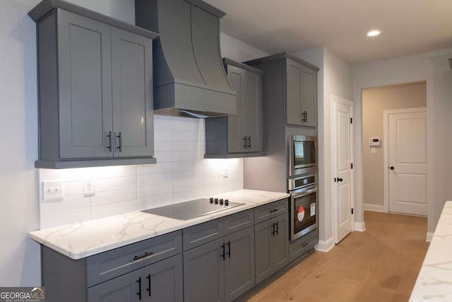 kitchen featuring appliances with stainless steel finishes, tasteful backsplash, custom range hood, gray cabinets, and light hardwood / wood-style floors