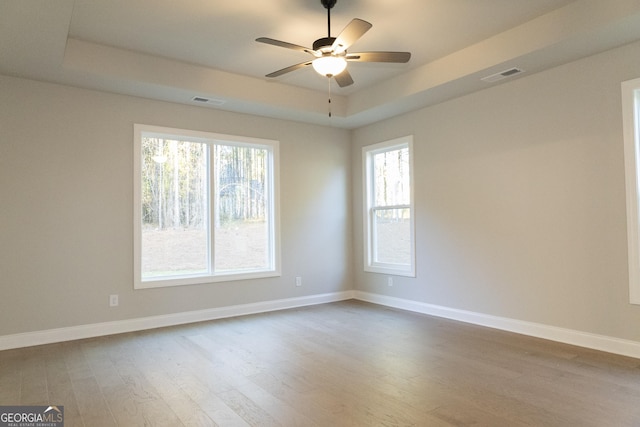 empty room featuring baseboards, visible vents, a raised ceiling, ceiling fan, and wood finished floors