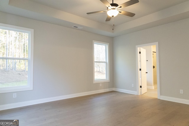 empty room featuring ceiling fan, visible vents, baseboards, a tray ceiling, and light wood finished floors