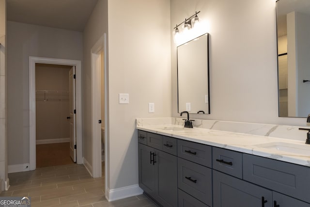 full bath with double vanity, baseboards, a walk in closet, and a sink