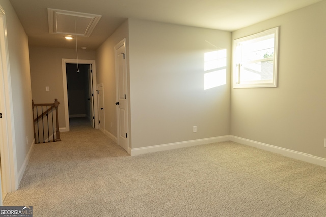 unfurnished room with baseboards, attic access, and light colored carpet