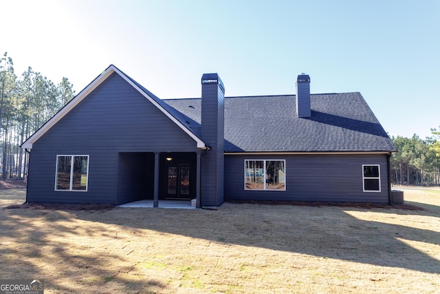 back of house featuring a lawn, a patio, a chimney, roof with shingles, and central AC