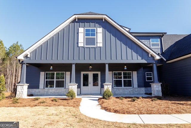 view of front of house with stone siding, a porch, board and batten siding, and french doors