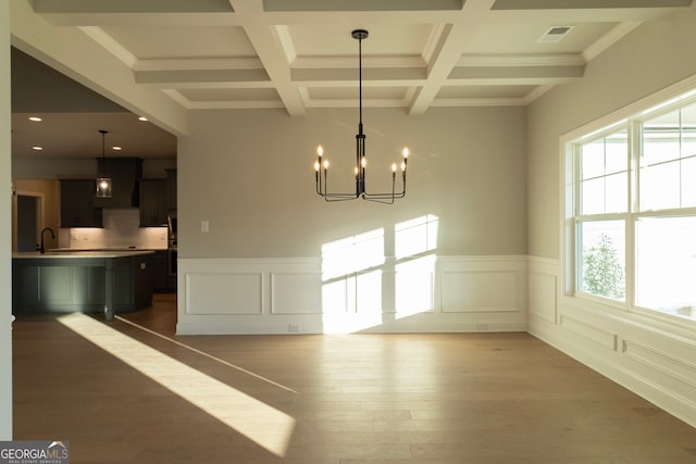 unfurnished dining area featuring dark hardwood / wood-style flooring, coffered ceiling, ornamental molding, sink, and an inviting chandelier