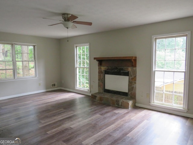 unfurnished living room featuring ceiling fan, wood-type flooring, and a stone fireplace