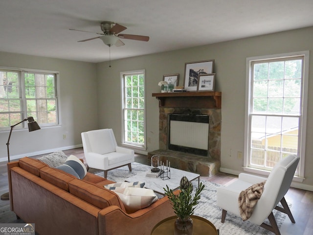 living room featuring ceiling fan, a stone fireplace, and light hardwood / wood-style floors