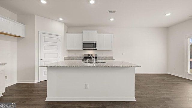 kitchen featuring light stone countertops, sink, dark hardwood / wood-style flooring, a kitchen island with sink, and white cabinets