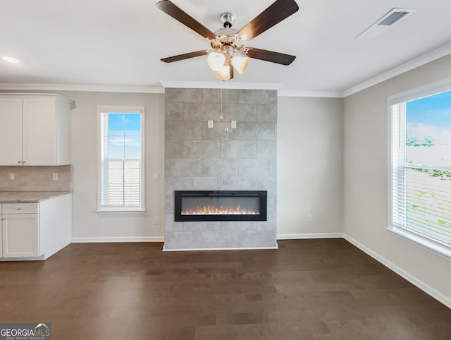 unfurnished living room with dark hardwood / wood-style flooring, a tiled fireplace, ceiling fan, and crown molding