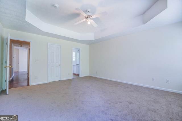 unfurnished bedroom featuring ceiling fan, light carpet, and a tray ceiling