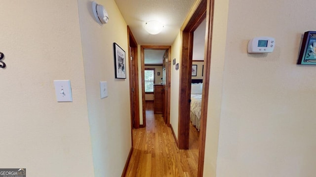 corridor with a textured ceiling and light wood-type flooring