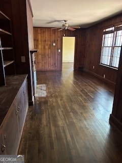 unfurnished living room with dark wood-type flooring, ceiling fan, and wood walls