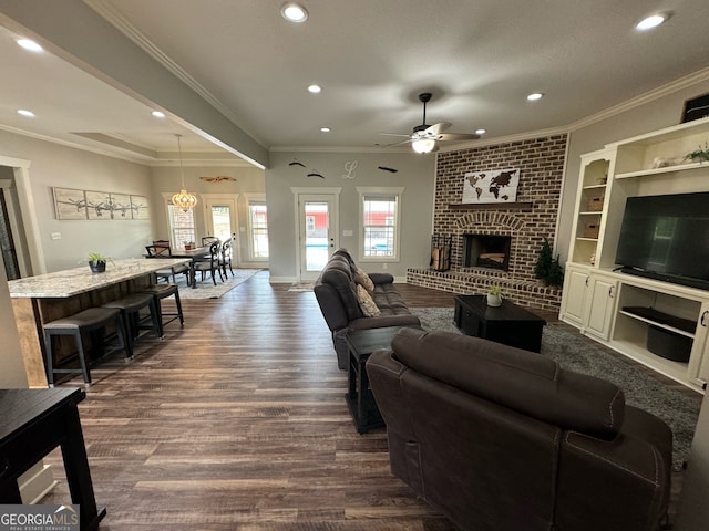 living room featuring crown molding, brick wall, dark wood-type flooring, a brick fireplace, and ceiling fan