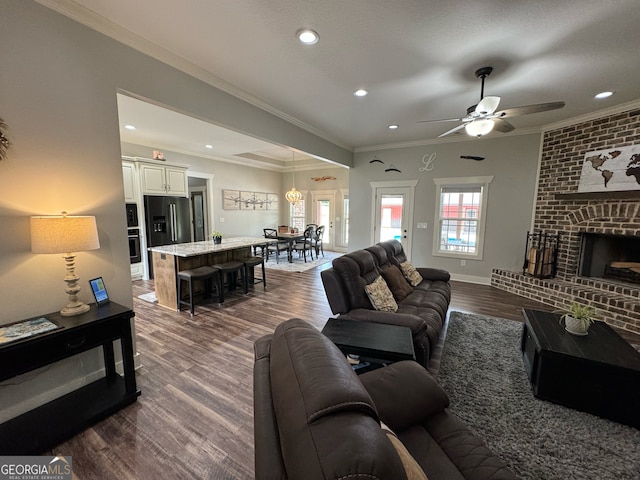 living room featuring brick wall, dark hardwood / wood-style flooring, a fireplace, ceiling fan, and ornamental molding