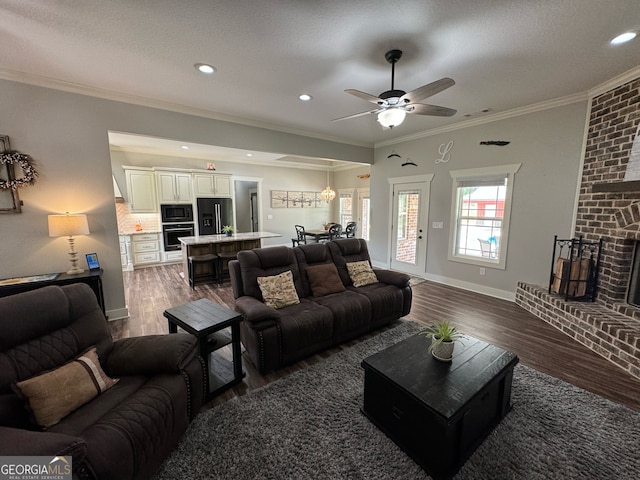 living room featuring dark hardwood / wood-style flooring, a fireplace, ceiling fan, crown molding, and a textured ceiling