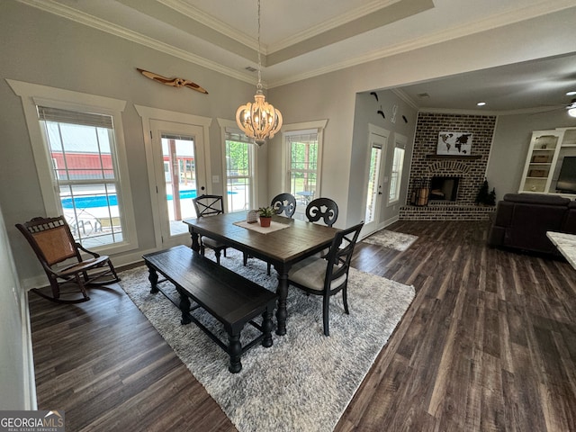 dining room with brick wall, ornamental molding, dark wood-type flooring, a brick fireplace, and a raised ceiling