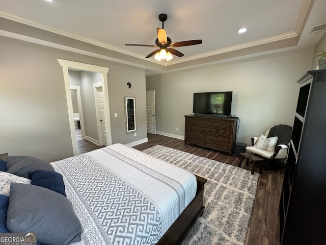 bedroom featuring ceiling fan, a tray ceiling, ensuite bath, and dark wood-type flooring