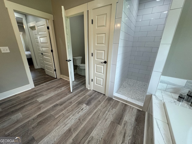 bathroom featuring wood-type flooring, a tile shower, and toilet