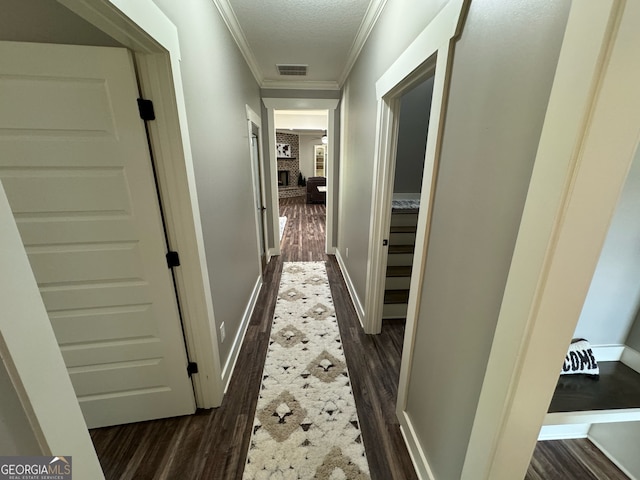 corridor with ornamental molding, a textured ceiling, and dark wood-type flooring