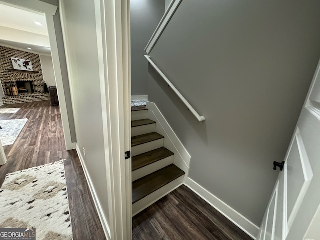 stairs with crown molding, dark wood-type flooring, brick wall, and a fireplace