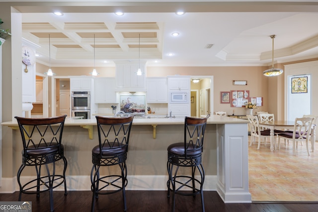 kitchen featuring white microwave, stainless steel double oven, hanging light fixtures, white cabinets, and a breakfast bar area