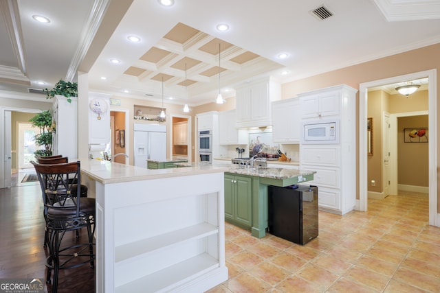 kitchen with coffered ceiling, a kitchen breakfast bar, a kitchen island with sink, built in appliances, and white cabinets