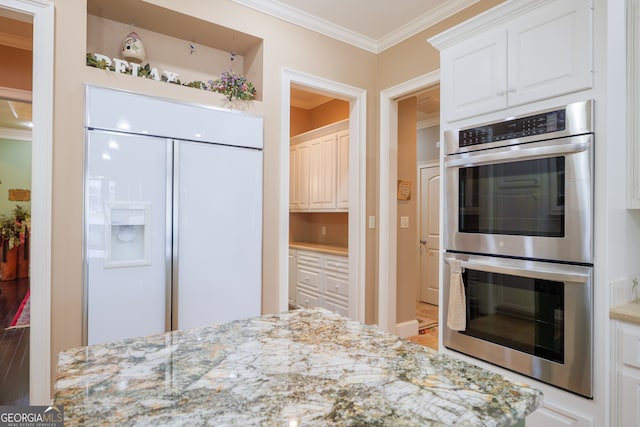 kitchen with white cabinetry, light stone countertops, ornamental molding, stainless steel double oven, and white built in refrigerator