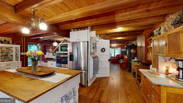 kitchen with hanging light fixtures, a healthy amount of sunlight, appliances with stainless steel finishes, and beamed ceiling