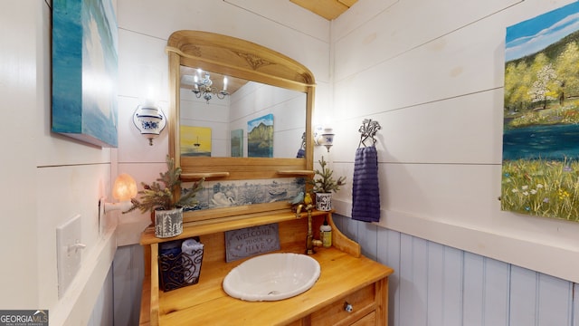 bathroom featuring wooden walls, an inviting chandelier, and vanity