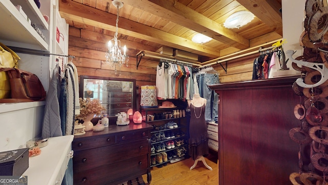 walk in closet with light wood-type flooring, a chandelier, and beamed ceiling