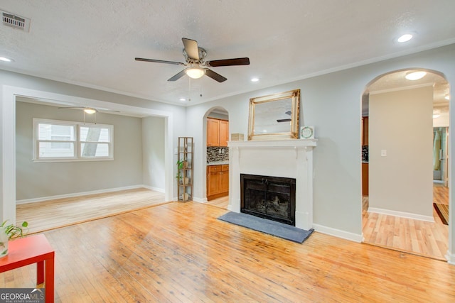 living room with ceiling fan, ornamental molding, a textured ceiling, and light wood-type flooring