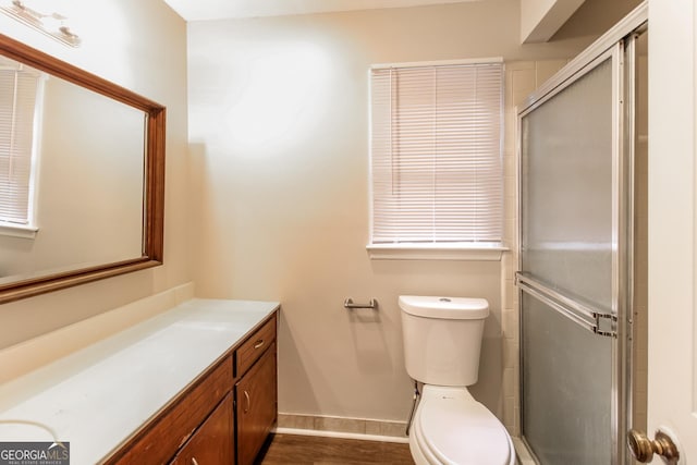 bathroom featuring baseboards, toilet, a shower with shower door, wood finished floors, and vanity