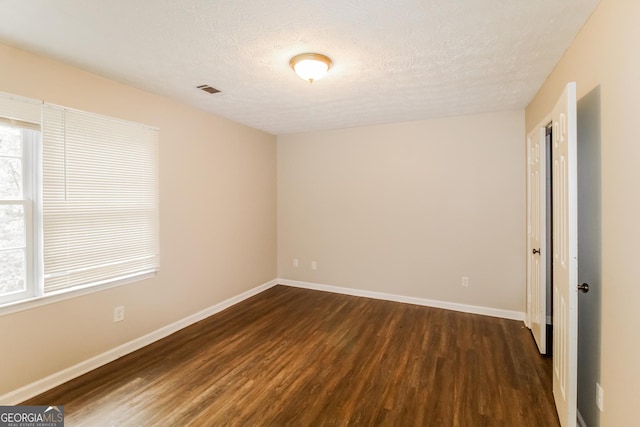 unfurnished room featuring dark wood finished floors, visible vents, baseboards, and a textured ceiling