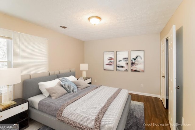 bedroom featuring visible vents, a textured ceiling, baseboards, and wood finished floors