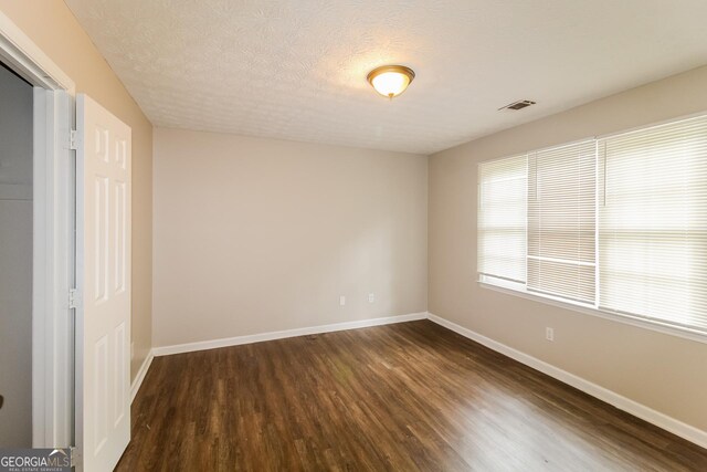 unfurnished room with visible vents, baseboards, a textured ceiling, and dark wood-style floors