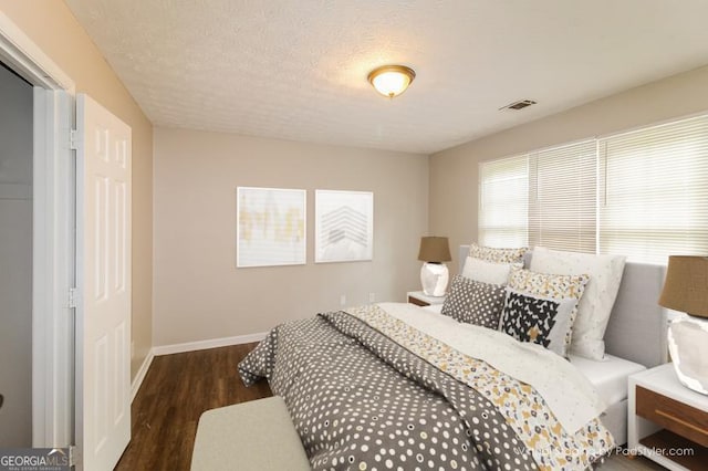 bedroom with visible vents, baseboards, a textured ceiling, and wood finished floors