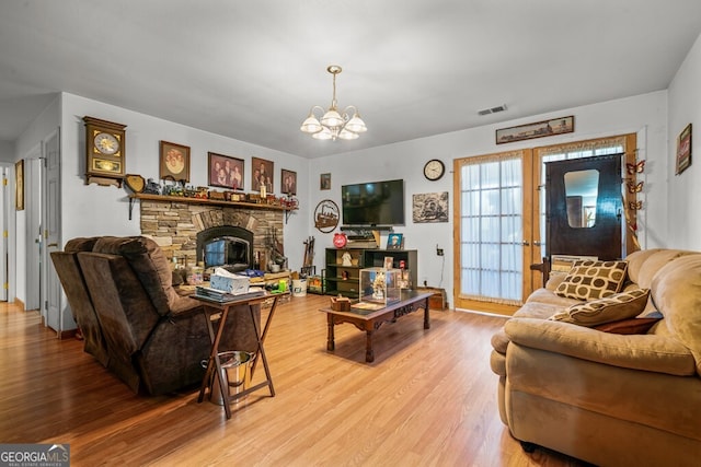 living room featuring a stone fireplace, light hardwood / wood-style floors, and a chandelier