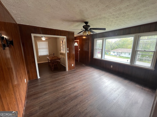 unfurnished living room featuring dark wood-type flooring, a textured ceiling, ceiling fan, and wood walls