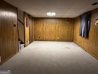 basement featuring a drop ceiling, wood walls, and light carpet