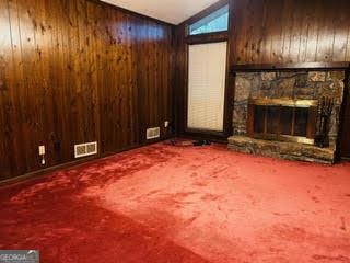 unfurnished living room with carpet flooring, vaulted ceiling, a stone fireplace, and wood walls