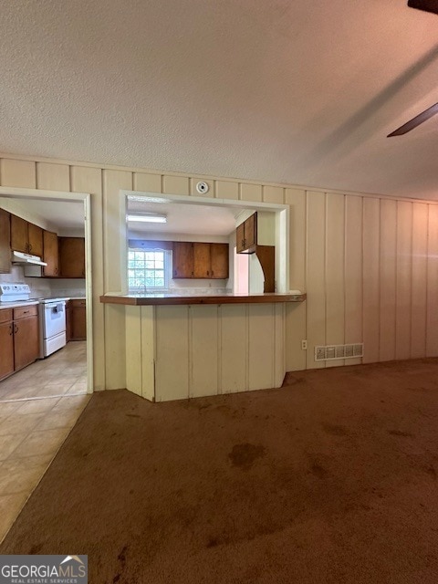 kitchen featuring white electric range, a textured ceiling, light carpet, and a kitchen bar